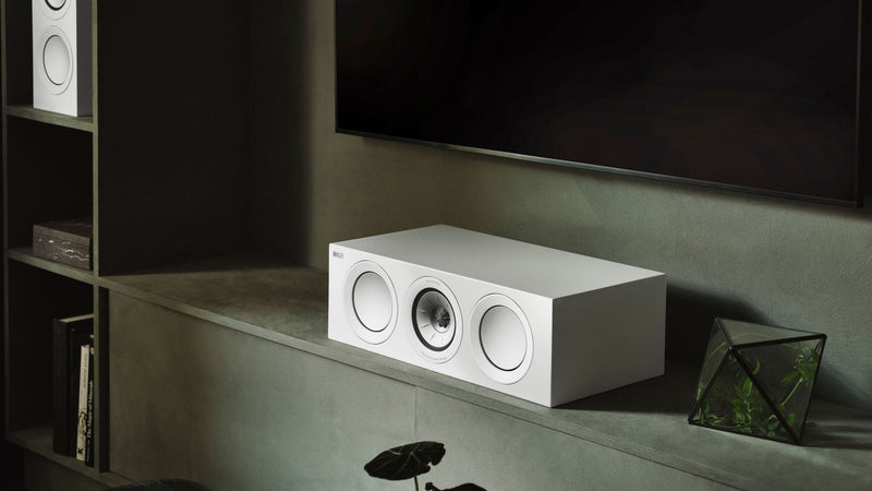 KEF R6 Meta centre channel speaker placed on table beneath a tv in a modern room
