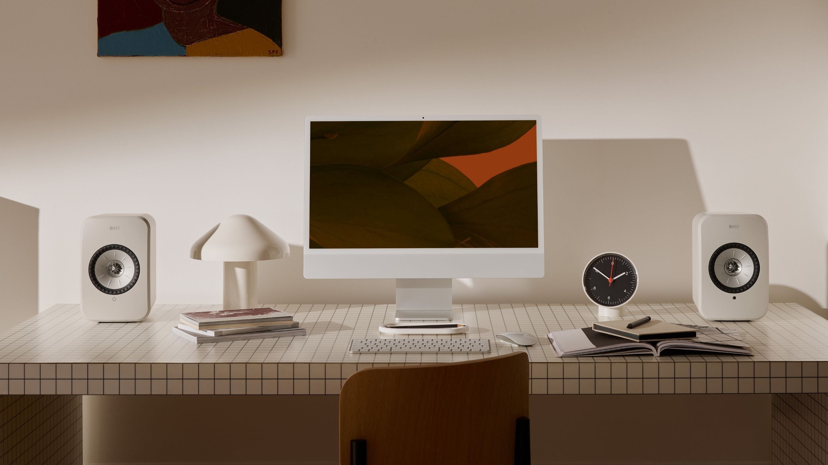 A desk featuring a computer, KEF LSX II LT Bookshelf speakers, and a stack of books, creating a workspace environment