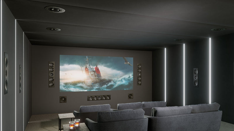 A spacious home theatre displaying a large projector screen, KEF architectural speakers, and a plush couch for an immersive experience.