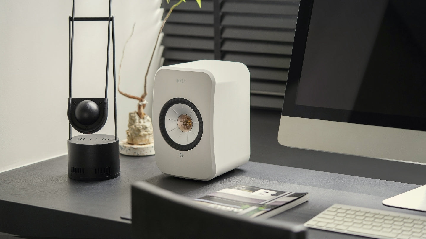 LSX speaker in white on work desk next to mac computer.